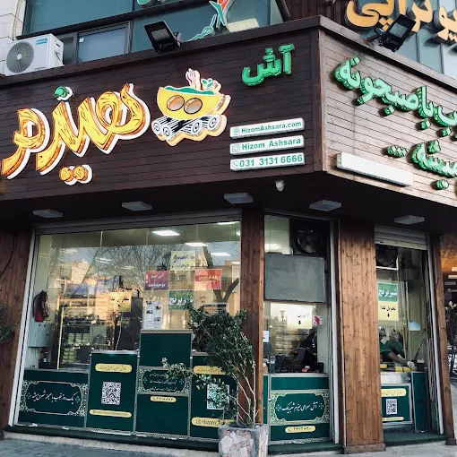 فضای داخلی رستوران با ستون آجری، میزهای چوبی و تابلوی نقاشی رنگی