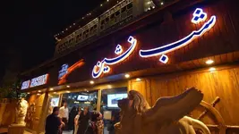 تابلوی نئونی رستوران شب‌نشین روی نمای چوبی ساختمان در شب